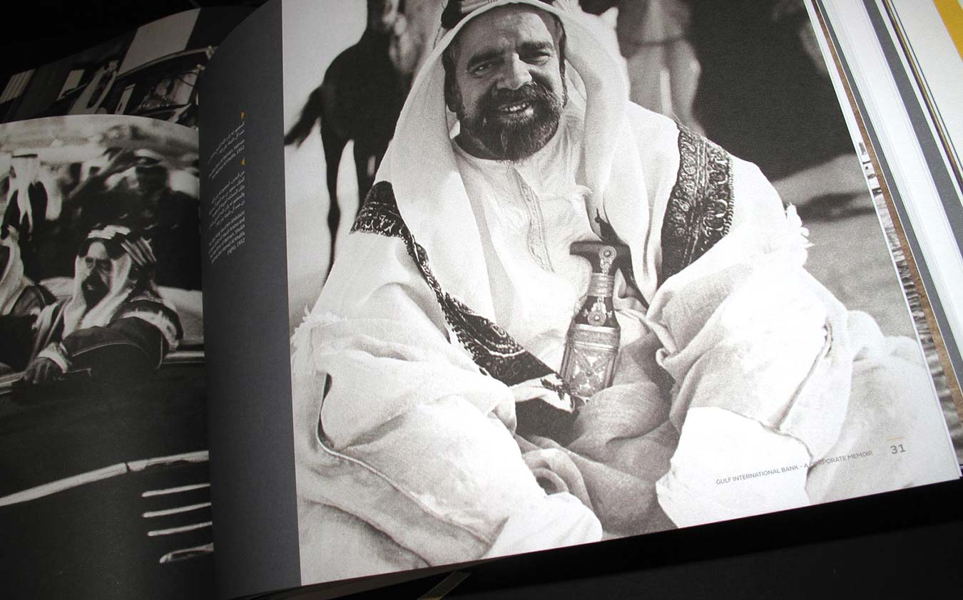 A large black-and-white historical portrait of a smiling Arab leader wearing a traditional ghutra and a decorative jambiya dagger tucked into his belt, displayed across an open corporate landscape brochure.