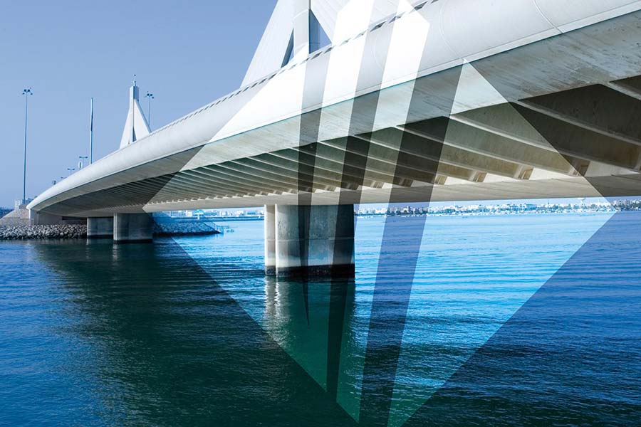 A wide-angle view of a modern cable-stayed bridge spanning across calm blue water, overlaid with a large, semi-transparent geometric diamond graphic containing three vertical stripes.