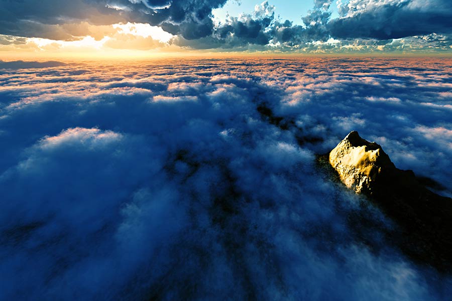 An aerial view of a mountain peak rising above a dense, dark sea of clouds, illuminated by the golden light of a sunset breaking through dramatic clouds on the horizon.