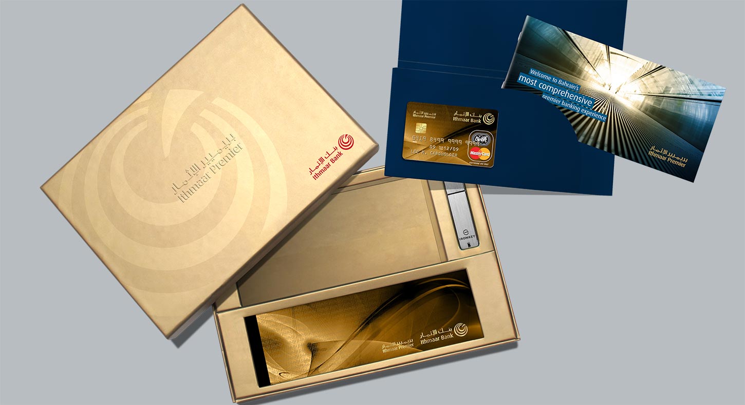 A premium welcome kit for Ithmaar Premier banking, featuring an elegant gold gift box containing a metal USB security device, a gold debit card presented in a dark blue folder, and an accompanying brochure detailing the banking experience.