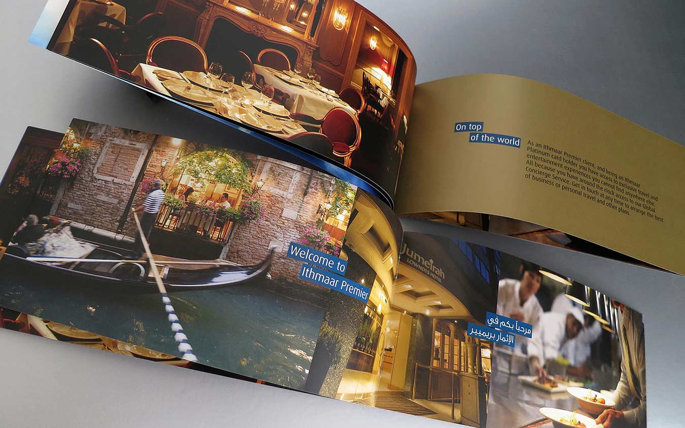 A marketing brochure spread for Ithmaar Premier banking, featuring a collage of luxury experiences including a fine dining restaurant, a gondola ride in Venice, the Jumeirah Lowndes Hotel, and professional chefs in a kitchen, accompanied by text detailing exclusive travel and entertainment privileges for cardholders.