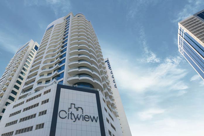 A low-angle shot of the white Cityview high-rise apartment building featuring its corporate logo on the exterior facade against a bright blue sky.