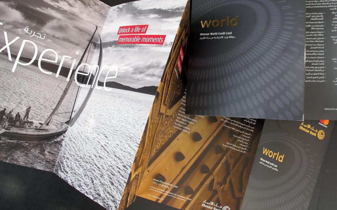 A marketing spread for Ithmaar Bank featuring a large photograph of a sailboat on the left with the text "Experience: Unlock a life of memorable moments," alongside brochures for the "Ithmaar World Credit Card" that highlight banking services, the bank's logo, and contact details.