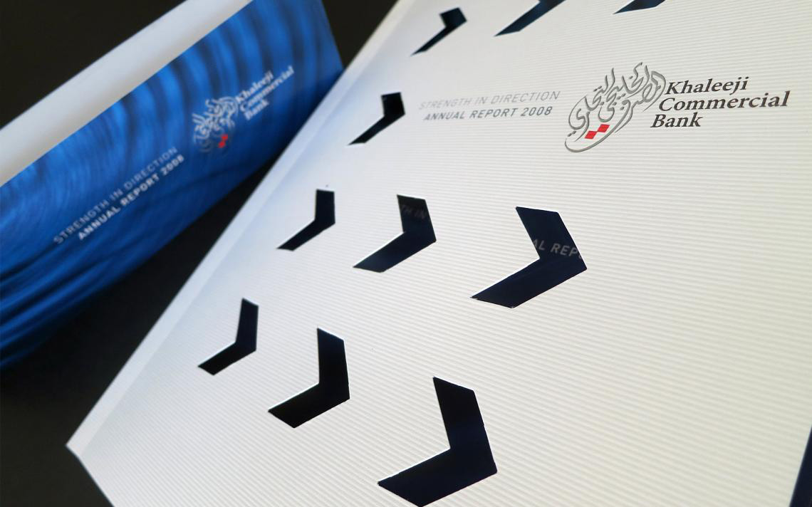 the presentation of the Khaleej Commercial Bank 2008 Annual Report, themed "STRENGTH IN DIRECTION."  The design features a textured white outer slipcase or cover with die-cut chevron shapes pointing to the right. Through these cutouts, a dark blue inner page is visible. The bank's logo and the title text are printed on the upper right of the white surface, while a completely blue matching volume sits blurred in the upper left background.
