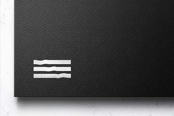 A close-up shot of a textured black card featuring a white, minimalist logo composed of three horizontal, slightly wavy parallel lines in the bottom-left corner.